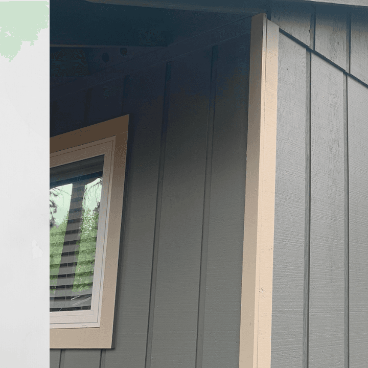 Close-up of gray vertical siding featuring tan trim around a window and corner board.