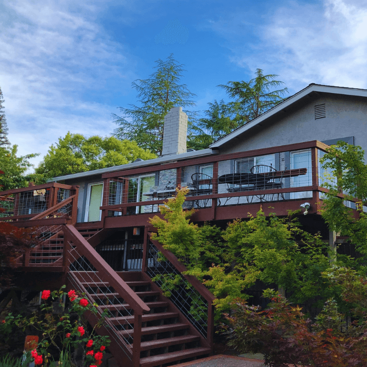 Wooden deck and stairs on a house surrounded by lush green trees and red roses.
