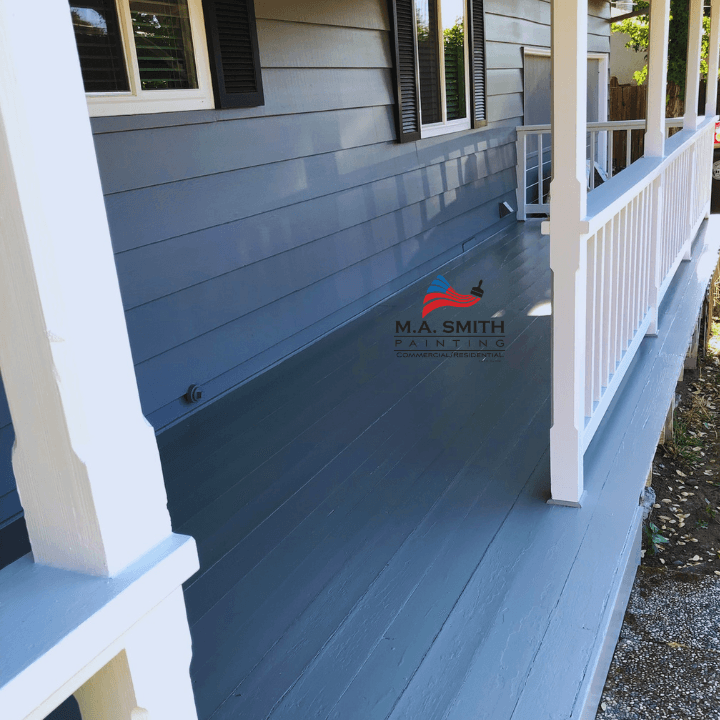 Freshly painted grey porch floor with white railings and blue-grey siding on a house.