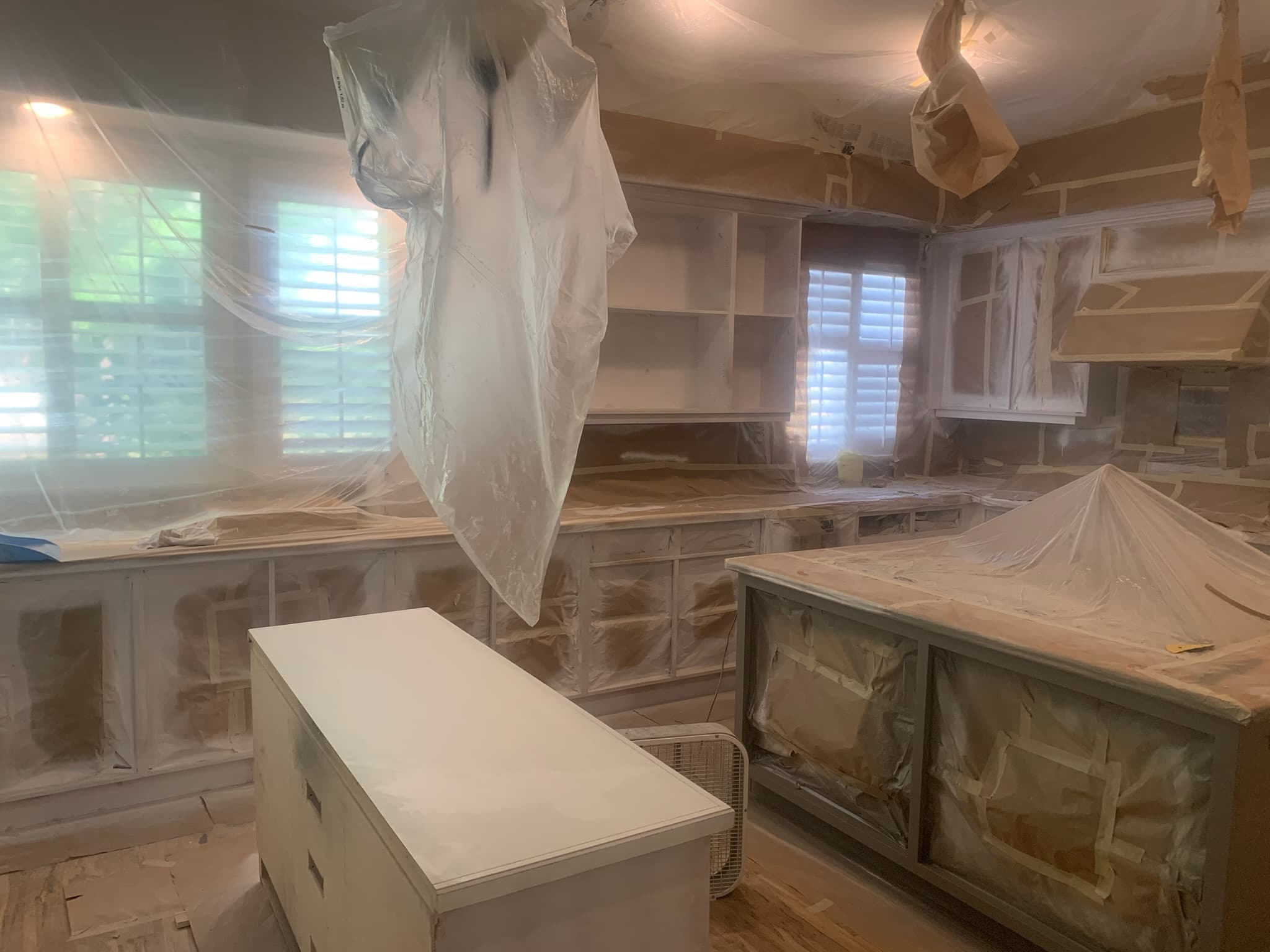Kitchen cabinets and surfaces covered in protective plastic and masking paper for a renovation.