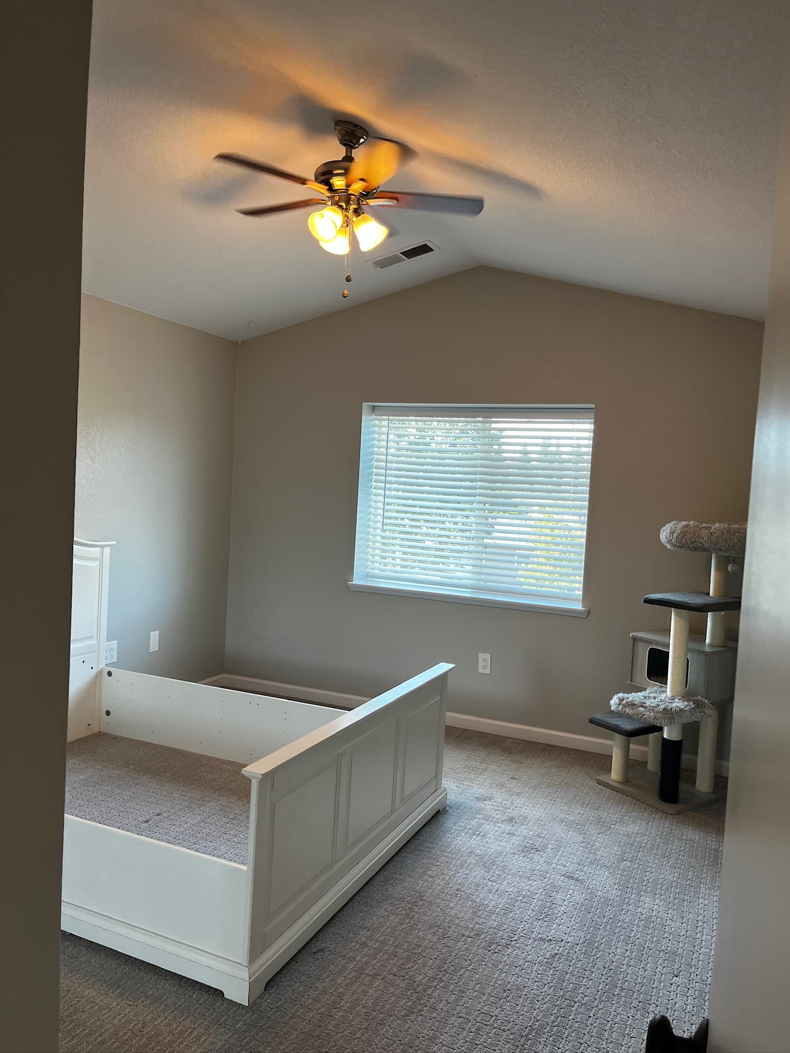 Empty white bed frame in a beige bedroom with a cat tree and ceiling fan.