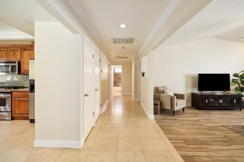 Bright home interior featuring a tiled hallway, kitchen with wood cabinets, and living room.