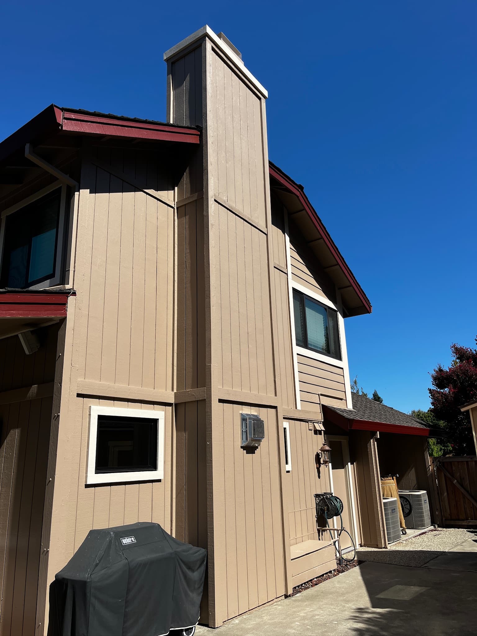 Tan two-story house with a large chimney, red trim, and a covered grill outside.