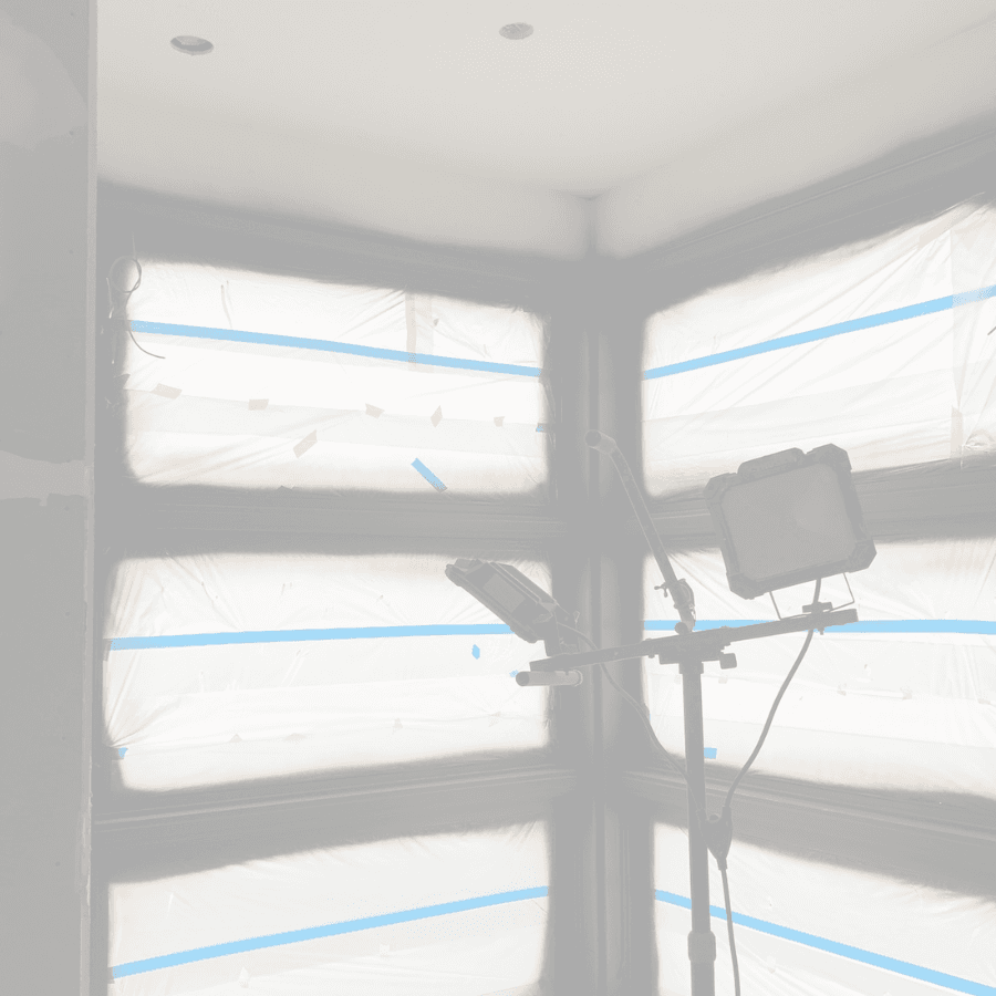 Bright work light illuminating windows covered in plastic sheeting and blue painter's tape.