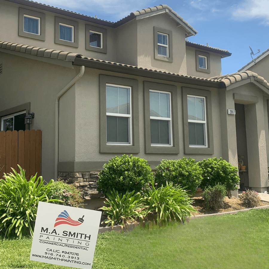 A beige two-story house with a painting company sign on the front lawn.